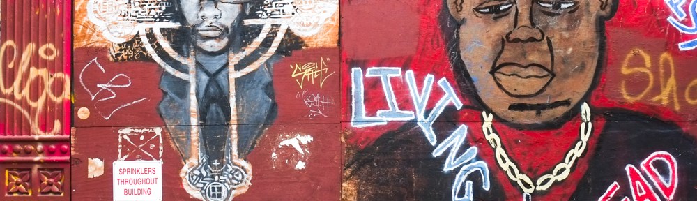 graffiti on a wall painted red, a white cross with a black man's face in the middle, portrait of another black man with words living dead