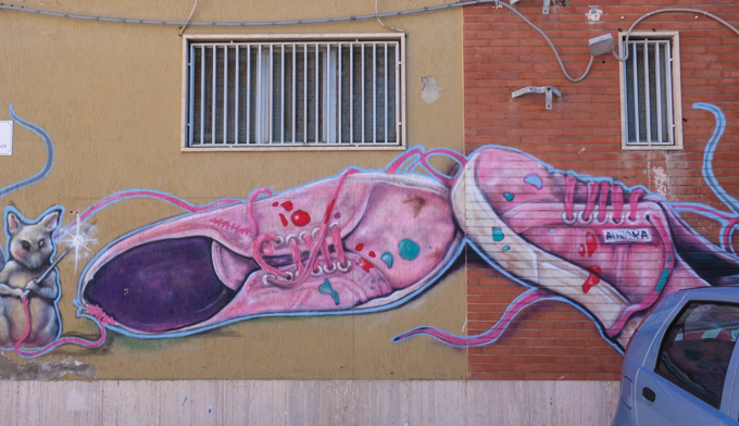 pair of pink running shoes with laces, mural painted by Aurora Agrestini, on a wall, with two windows 