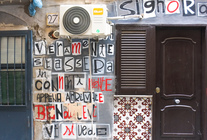 words pasted letter by letter on the side of a wall between two doors of residences, Naples, 