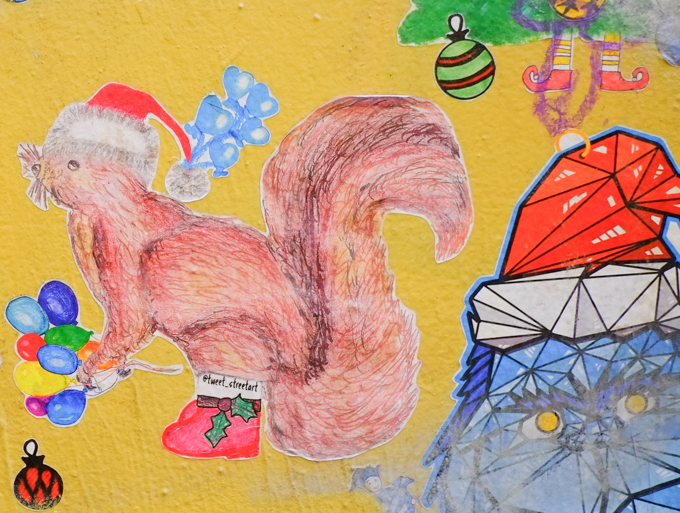 christmas themed graffiti, squirrel by tweet streetart wearing a red hat and red boots with holly on them, carrying a bunch of balloons, also the grinch wearing a Santa hat, 