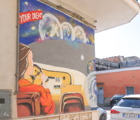 mural with text, your dream, woman driving a car, moon and planets and swirly clouds outside the window