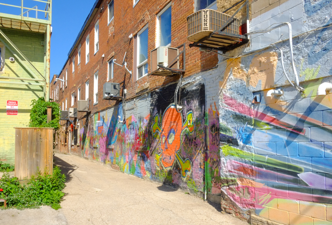 alley behind shops in Owen Sound, three storey brick buildings with street art murals along the bottom third.