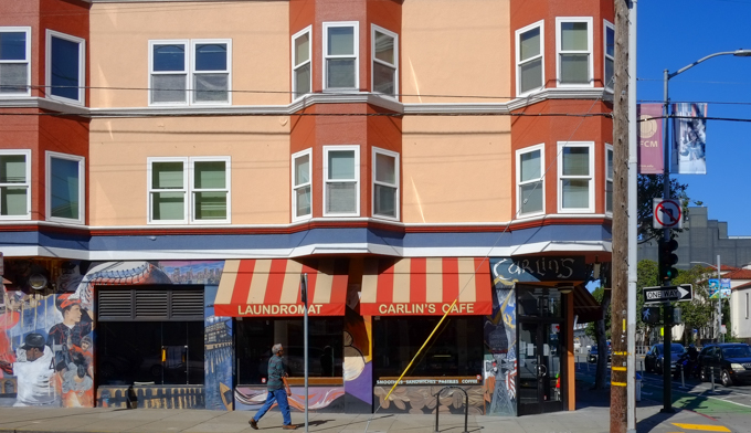 street view of Carlins Cafe an Laundromat on Valencia Street in the Mission District of San Francisco, orange and yellow awnings over two large window, 