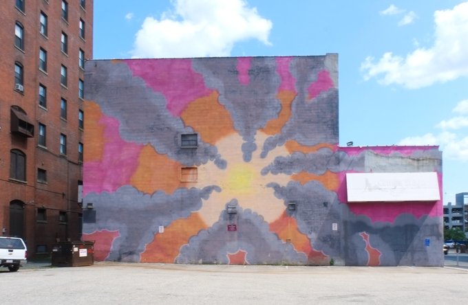 Colorburst type of mural yellow in center, with rays radiating from center in pink and orange, gray background