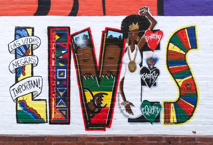 close up on word lives in a black lilves matter mural.  pictures and patterns in the letters.  Las Vidas Negras Importan!, also hearts with empathy, energy, equality written in them,also a black woman with gold crown and long white gown