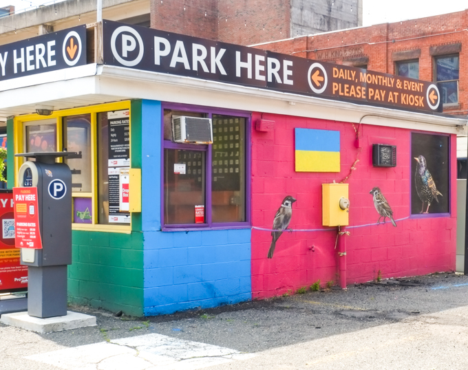parking lot kiosk building painted in bright colours with painting of 3 birds on a wire