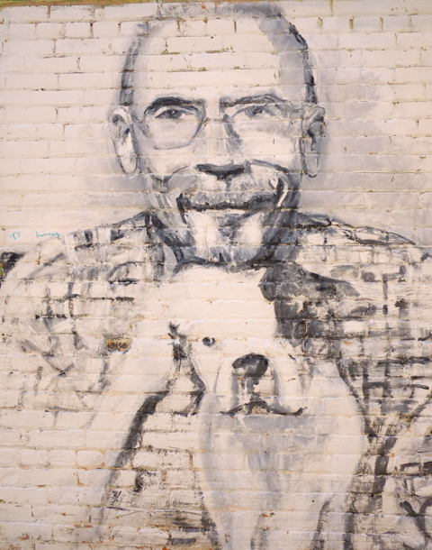 street art black and white portrait of an older balding man with his dog. Small dog is white with black patch covering one side of face