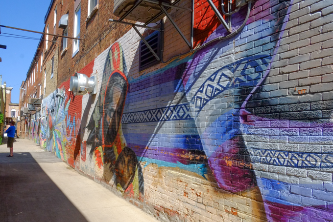 alley behind shops in Own Sound, three storey brick buildings with street art murals along the bottom third. Purple stripes