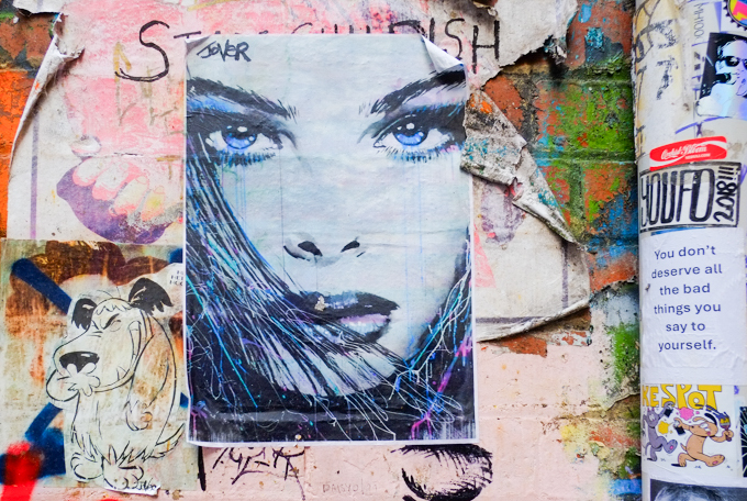 You don't deserve all the bad things you say to yourself text on a sticker, also a paste up by Jover of woman's face, with blue eyes, 