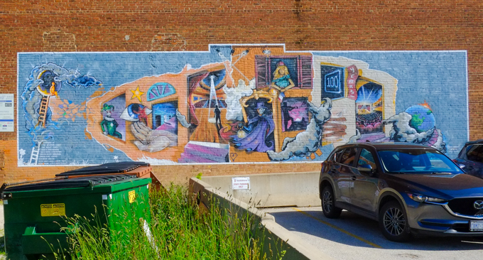 car in parking lot, parked in front of a large theatre themed mural painted on the back of a cinema