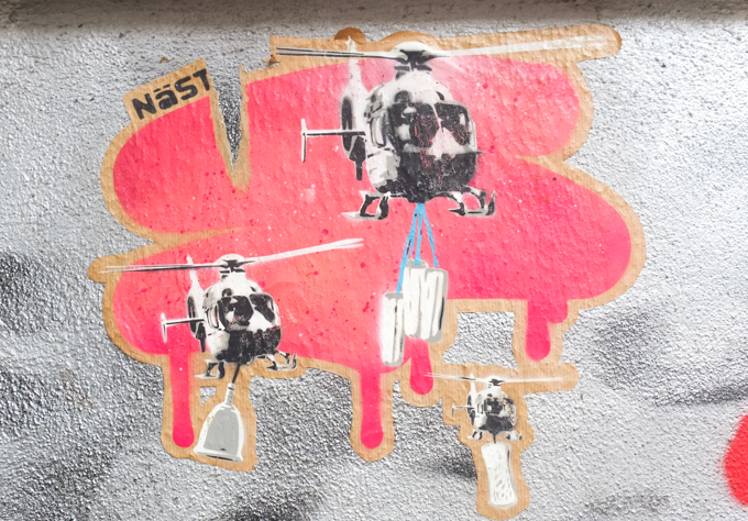 on red background, graffiti of three helicopterd in flight, each carrying something, all feminine hyguene products, tampons, a rolled up pad, and a menstrual cup. 
