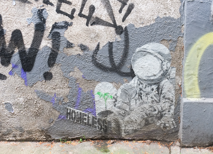 paper paste up, printed image of astronaut sitting on the ground with a sign in front of him that says homeless.