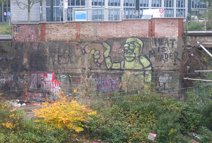 rough street art painting in Dusseldorf Germany, green male figure holding a sausage in one hand, text on painting says meat is murder