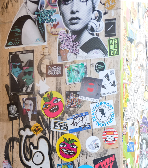 many stickers  pasteups on a wall in Cologne,   The corona brothers, nane apple faces, paradoxon, black and white women's portraits, 