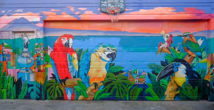 large mural covering garage front, parrots, macaws, toucan, and other birds, also a Jesus with woman and baby. 
