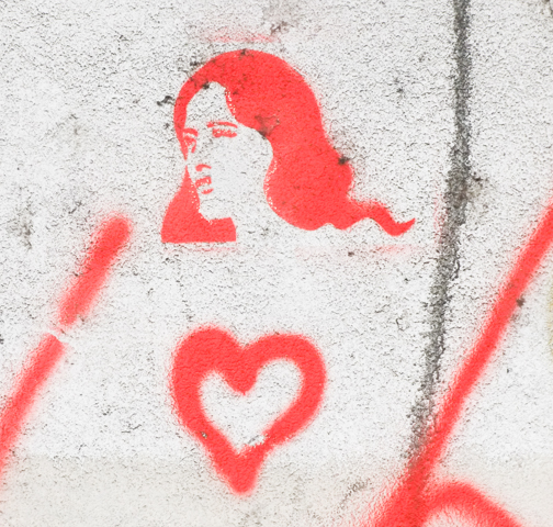 red stencil of a woman with long hair, seen in profile, also a small red heart beneath the portrait 