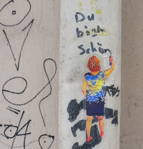 paste up graffiti, a red headed woman in a blue skirt is spray painting on a wall 