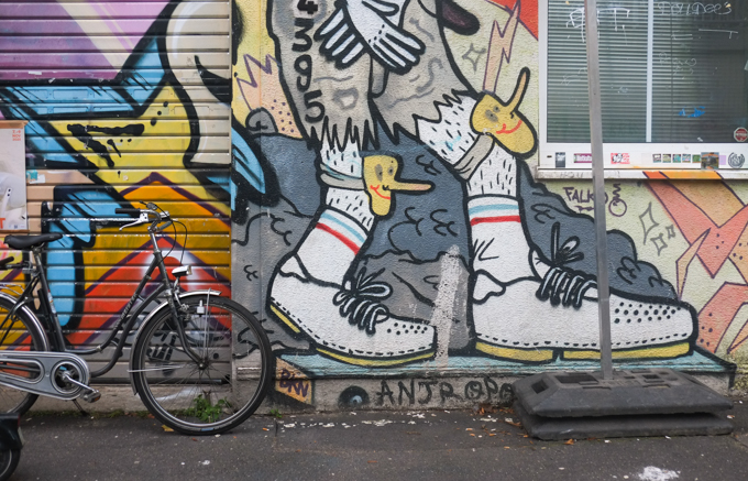 street art on Hochstadenring in Bonn Germany - lower part of a mural, big feet with white socks and laced shoes, yellow knee pads that look like faces with long noses.  Urban art by Falko.