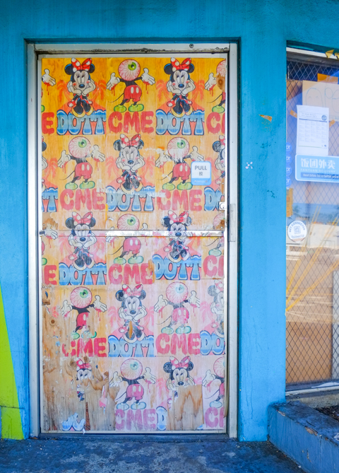 boarded up glass door covered with mickey mouse and minnie mouse images, some with giant eyeball oozing instead of a head