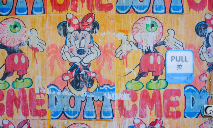 portion of boarded up glass door covered with mickey mouse and minnie mouse images, some with giant eyeball oozing instead of a head, with pull sign with chinese alphabet characters