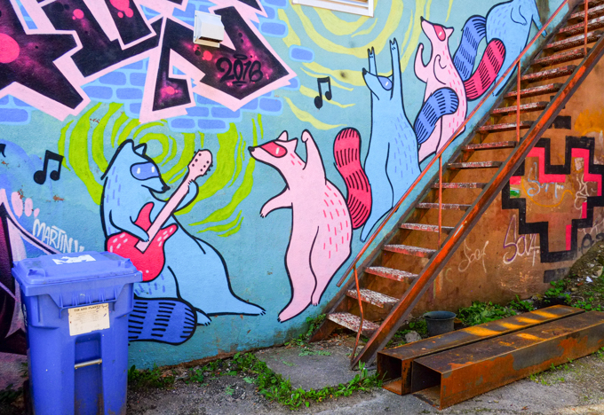 pink and blue raccoons, one playing a guitar, the others dancing on the stairs.