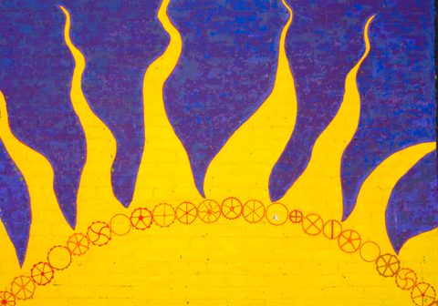 small street art painting of a semi circular yellow sun with long rays, symbols underneath