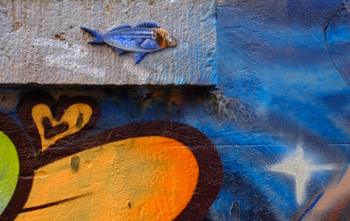 small three D fish graffiti on a wall, beside a painted yellow heart with happy face on it 