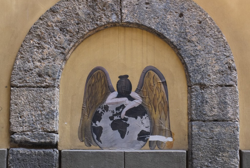 paste up graffiti of an angle with large wings as she leans on a globe, with north pole at the top