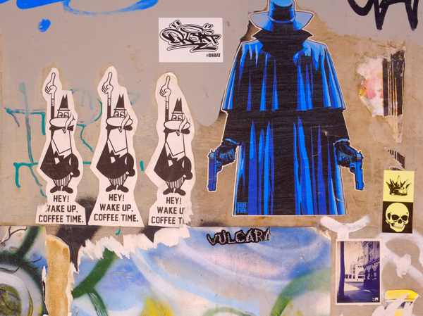 graffiti in Rankins Lane, Melbourne, paste ups of three little men saying hey, it's coffee time, also a very blue shadowy character with a gun in each hand and a long robe and hood that covers his face