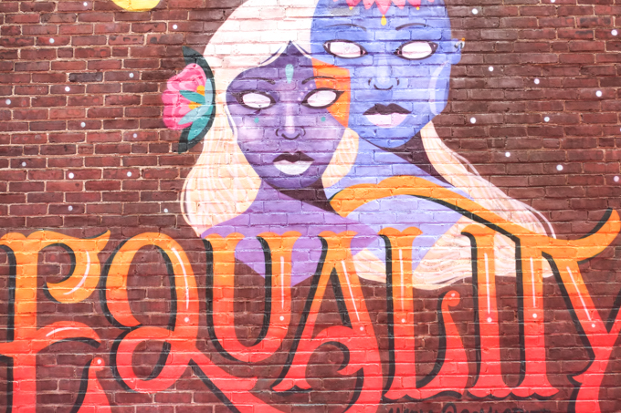 equality mural, two faces, purple female and blue male, woman has red rose in hter long white hair, man has basket of flowers on his head. 