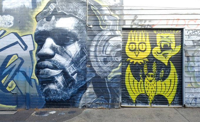 on the left, in grey tones, street art painting, portrait in greys of young man wearing large headphones and on the right, three yellow characters by dscreet, one of which looks like an owl