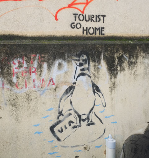 stencil graffiti in Palermo, a penguin carrying a suitcase, text that syas tourist go home