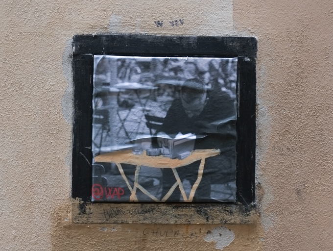 black and white photo of a man reading at a table outside, table has been painted orange