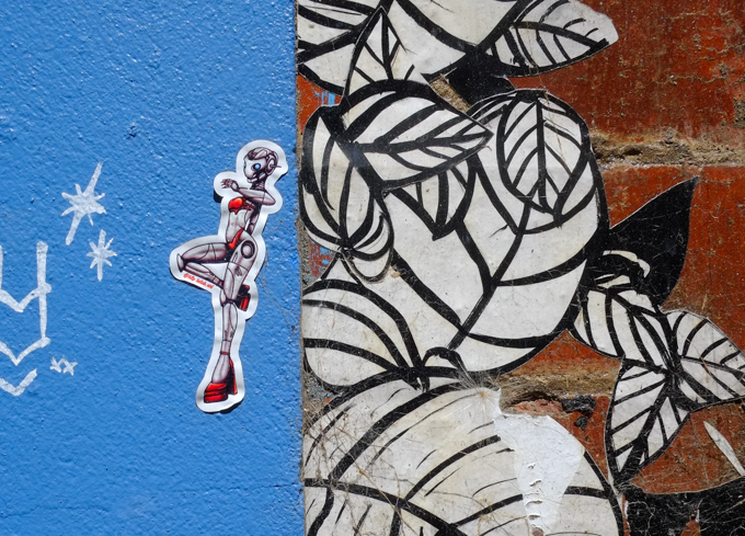 2 pieces of street art in Warburton Lane, Melbourne. Part of a painting of white leaves on black, one a slap by leilah of a cat-like woman robot with high red shoes and bikini