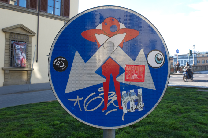 modified traffic sign, graffiti, by Clet Abraham, in Florence, two arrows wrap around neck of figure, trying to strangle him