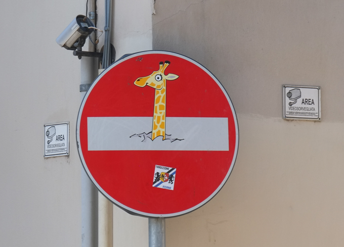 modified traffic sign, graffiti, by Clet Abraham, in Florence, long neck of giraffe poking above white bar