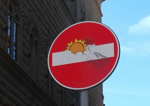 modified traffic sign, graffiti, by Clet Abraham, in Florence, sun breaking through the cloud cover