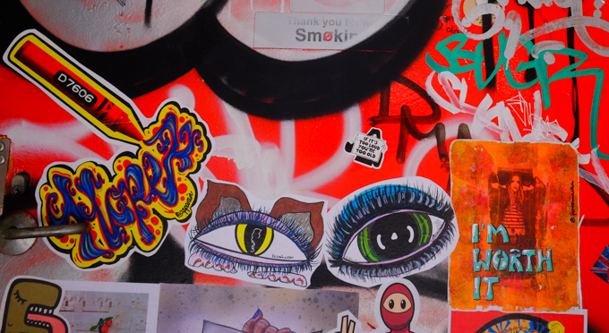 graffiti paste ups and stickers on a wall, D7606 crayon, eyes, a sign that says I'm worth it