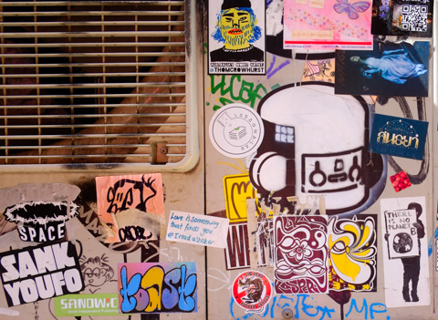 collection of graffiti stickers and paste ups on a wall