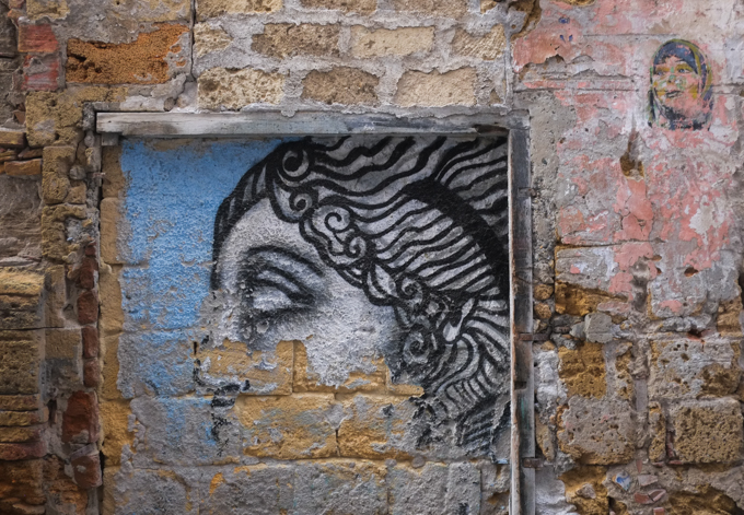 two women's portraits, faded street art on an old brick and stone wall, textures, alley in Palermo