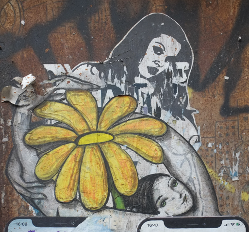 paper  paste up graffiti of two young woman in grey tones, with a large yellow daisy flower