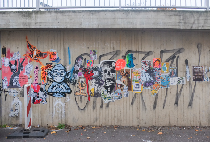 concrete wall between street and elevated section of road, with many graffiti slaps and paste ups on it, Bonn Germany