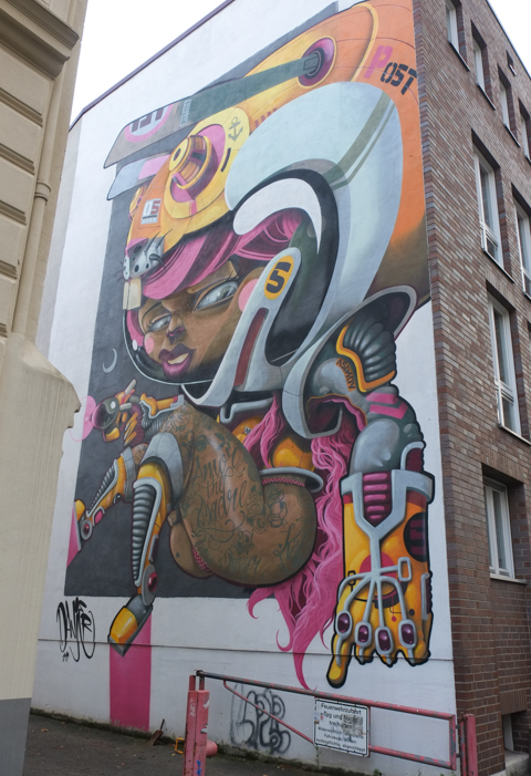 large mural in Nippes Cologne, by Danjer Mola, of a female astronaut with either bare legs or brown skin tight leggings, 