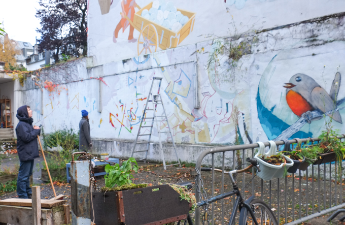 artist with ladder preparing a wall for mural painting, lines drawn on wall, a painting of a bird already exists beside the spot