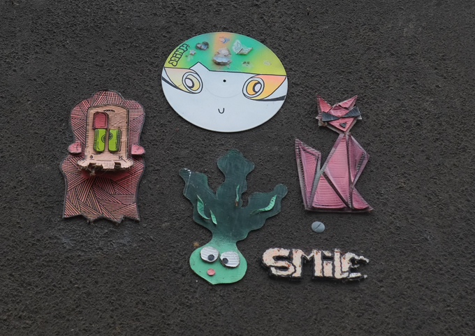 black wall, graffiti, 4 small pieces, by JoinyStreetArt (round white face), sm111le (smiling radish), Karl Heinz Swaggert (hairy fellow on the left), and Metraeda (pink cat)