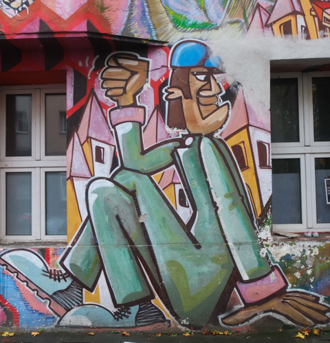 man, dressed in green with blue shoes and blue cap, sitting on the ground, seems to be yelling