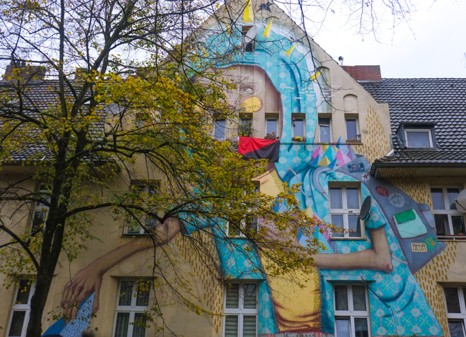 upper part of mural, behind a tree, person in blue head scarf, holding something yellow and large, 