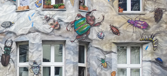 4 storey residential building covered in paintings of insects, beetles, ants, and others both real and imaginary crawling around between the windows, mural in Dusseldorf, some insects have human faces