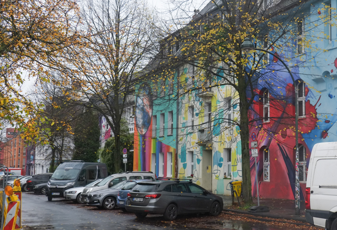 row of buildings, 4 storeys, all covered with different colourful murals, kiefernstrasse (pine tree street) in Dusseldorf Germany