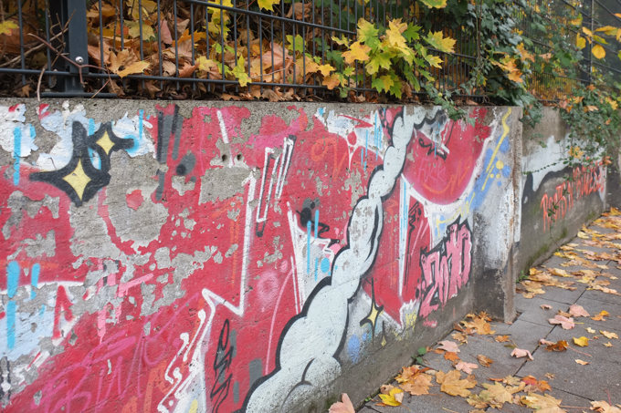 concrete fence, low, with metal bars above, autumn leaves, old painting from 2010 on the concrete, red background, 